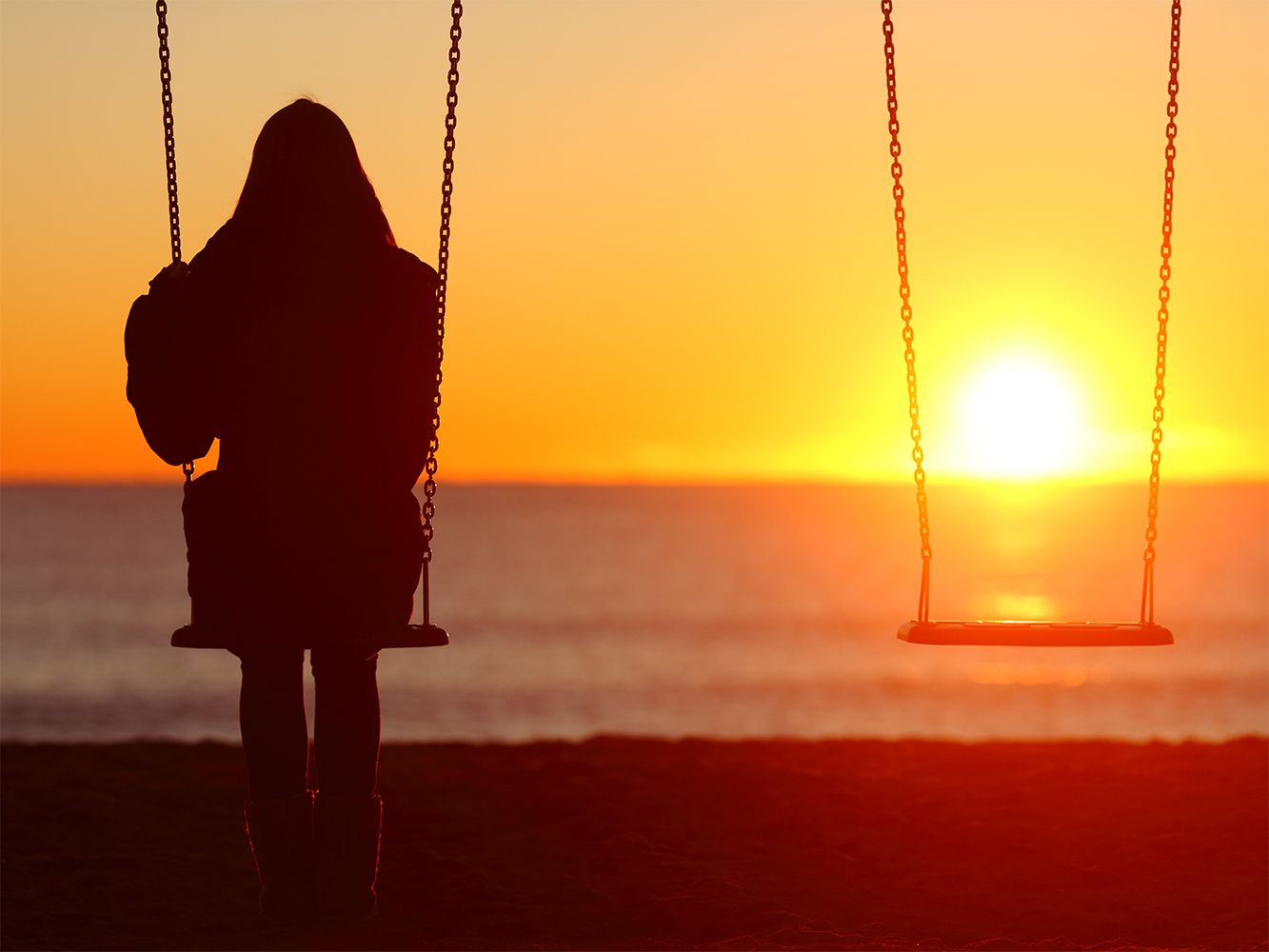 Frau auf einer Schaukel am Strand und der Sonnenuntergang im Hintergrund